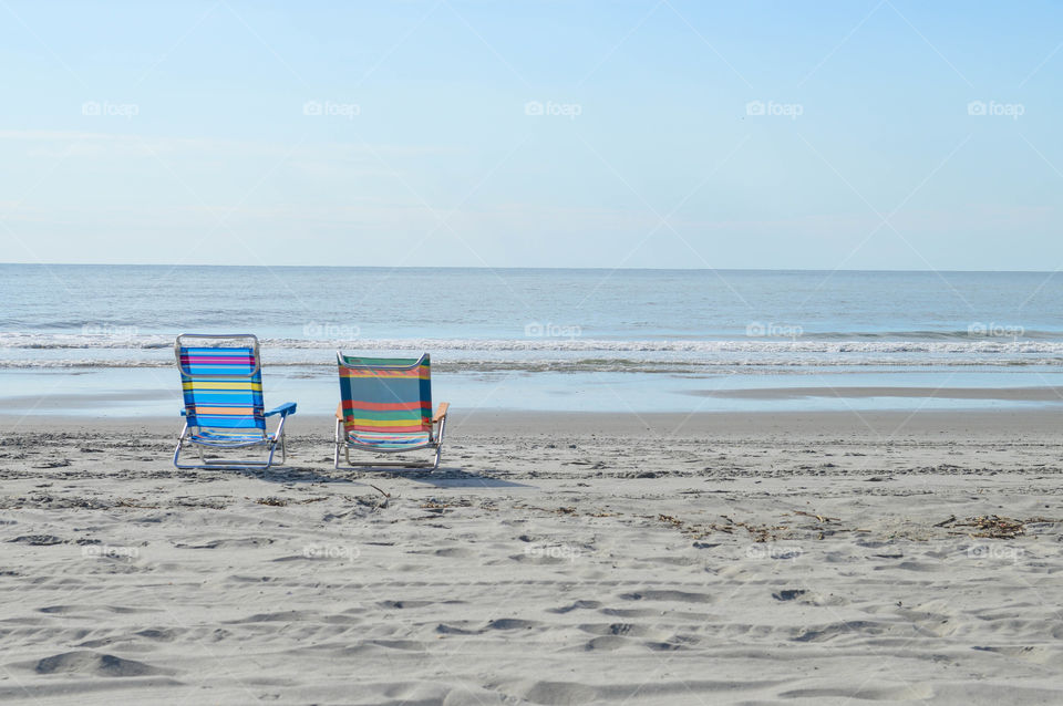 Two empty, colorful lounge chairs on the beach overlooking the ocean