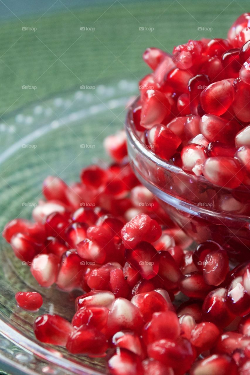 Closeup of fresh pomegranate seeds overflowing a small glass bowl against a green background