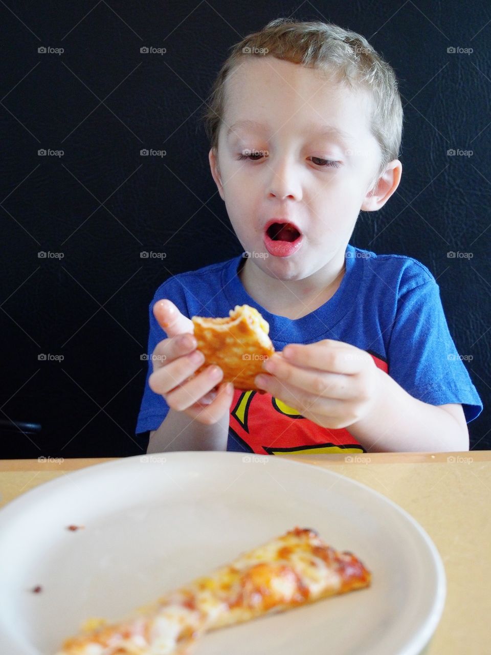A little boy is shocked by his favorite food of pizza as it’s very hot fresh from the oven. 