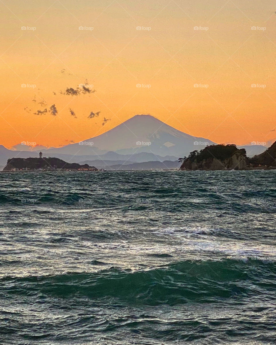 Beautiful orange glow sunset with mountain (Mt Fuji) and islands, dark ocean in the foreground with waves.