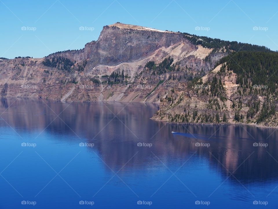 The rich blue waters of the deep Crater Lake in Southern Oregon with fir trees on the jagged rim on a beautiful sunny summer morning with clear blue skies. 