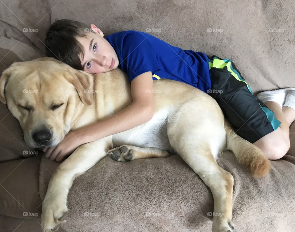 A boy and his dog are very cozy resting on the couch 