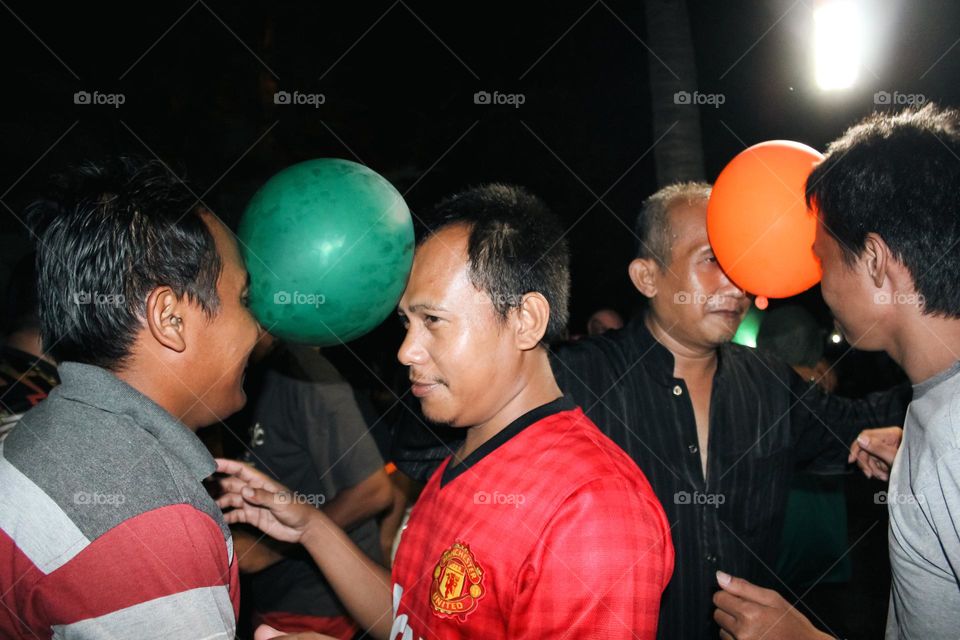 Close up of a group of men looking happy doing a dance game with balloons attached to their heads, a teamwork game to build a great team.