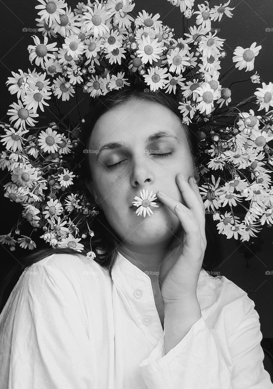 original, conceptual black and white portrait of a woman with a daisy wreath on her head and a daisy near her mouth