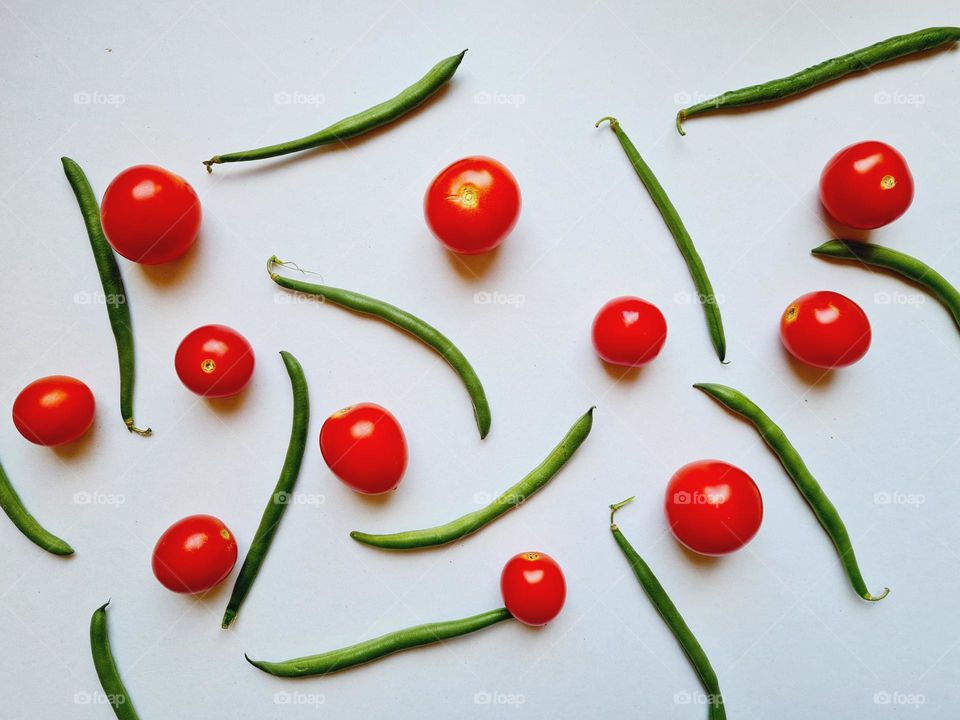 cherry tomatoes and green beans scattered on white background