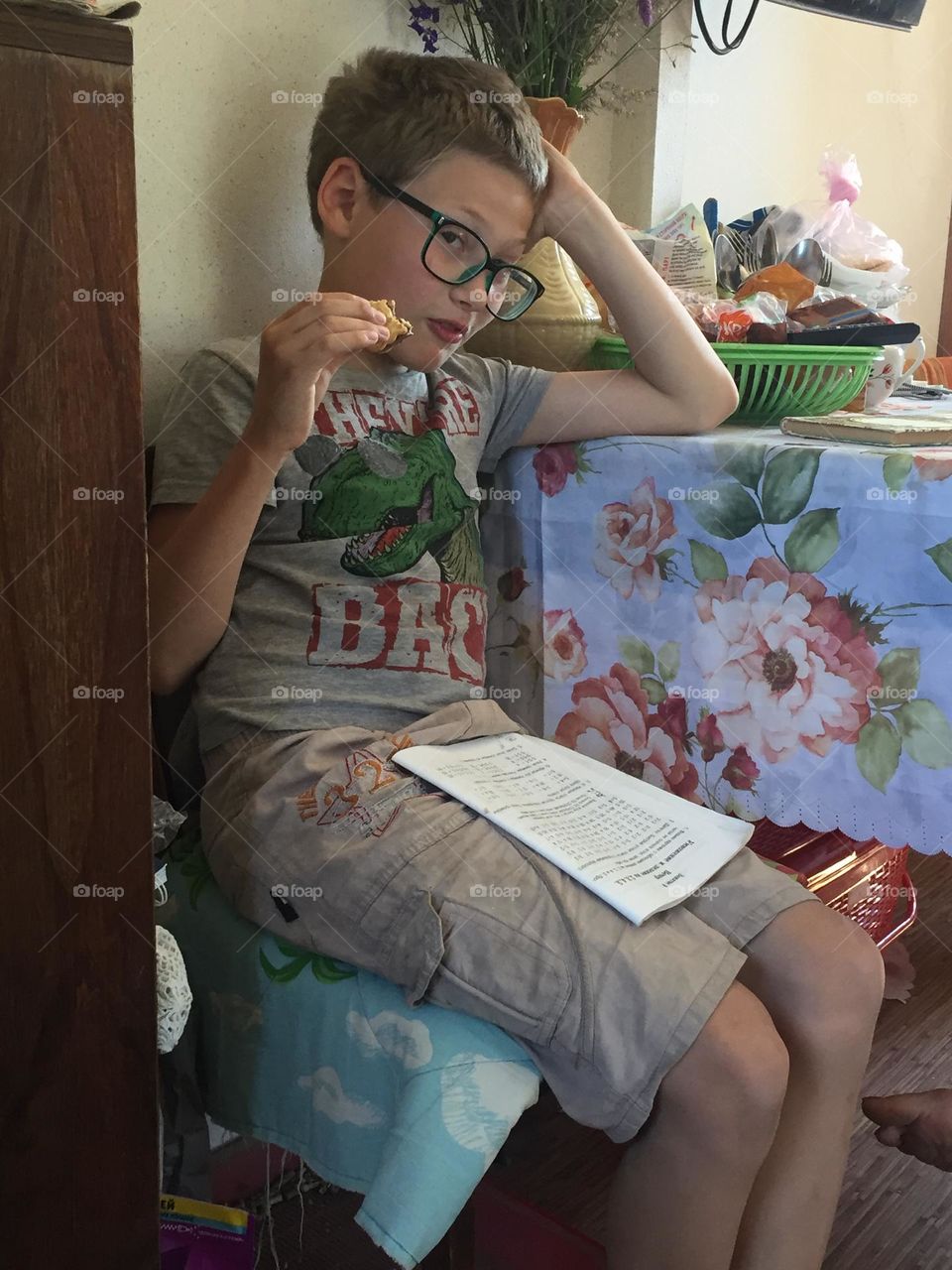 Teenager boy in glasses sits at a table and reads