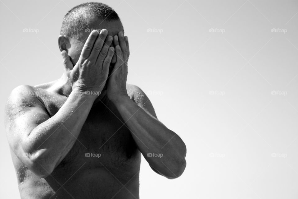 Portrait of man hiding his face: after having swam or because of crying? We don’t know. 