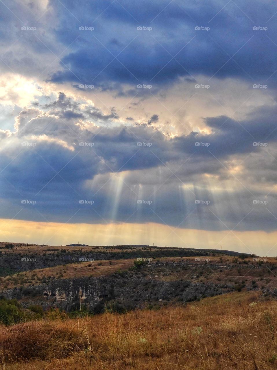 An amazing photograph of the hills landscape in Bulgaria in the summer with beautiful colours, clouds and sun rays shining through them