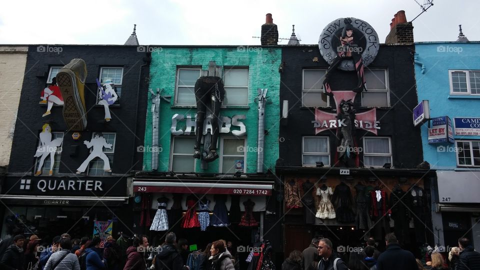 An eclectic colourful row of shops in Camden Town as statues of art tower over the people