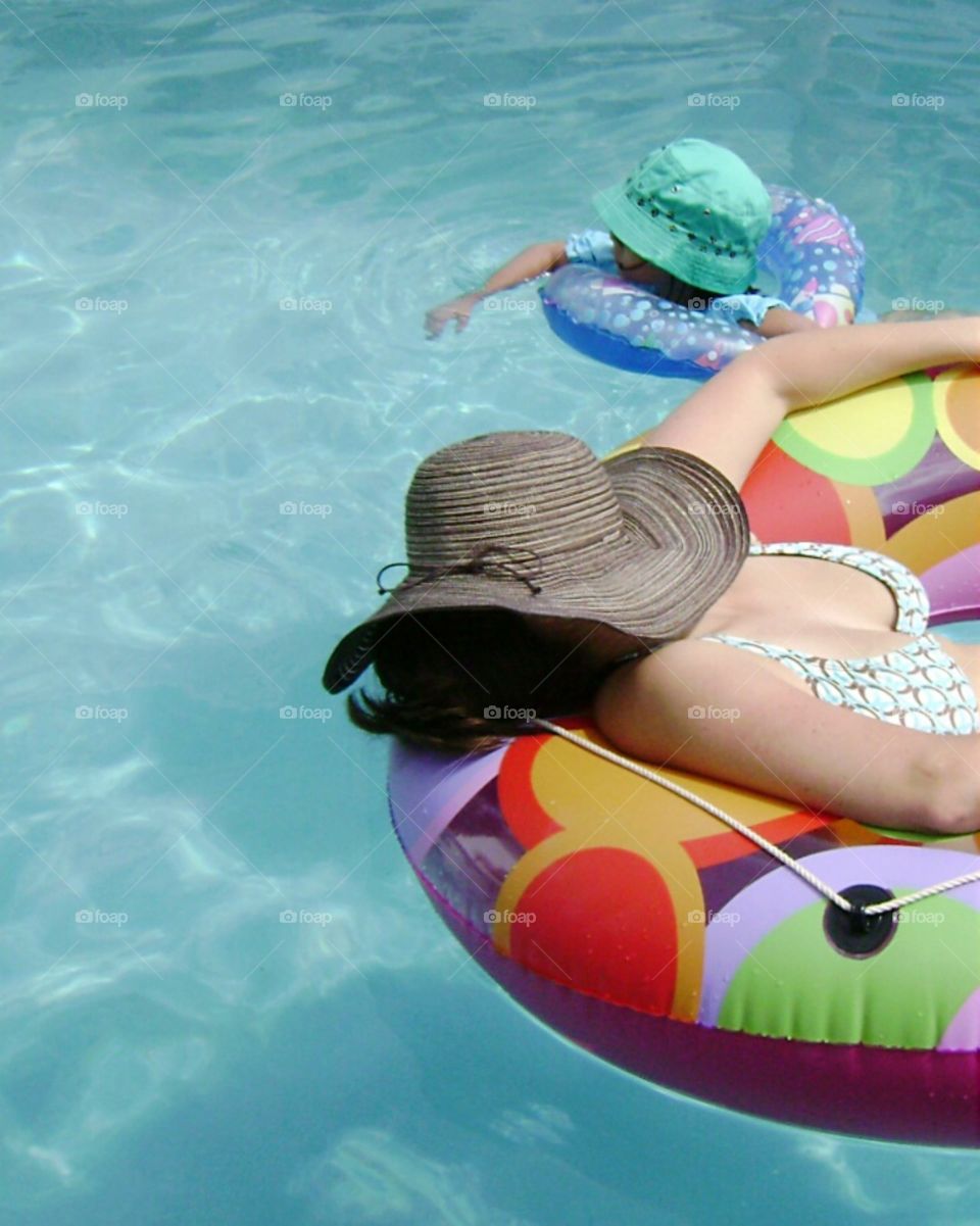 pool time. Mother and daughter spending time in the pool; both in hats and innertubes.