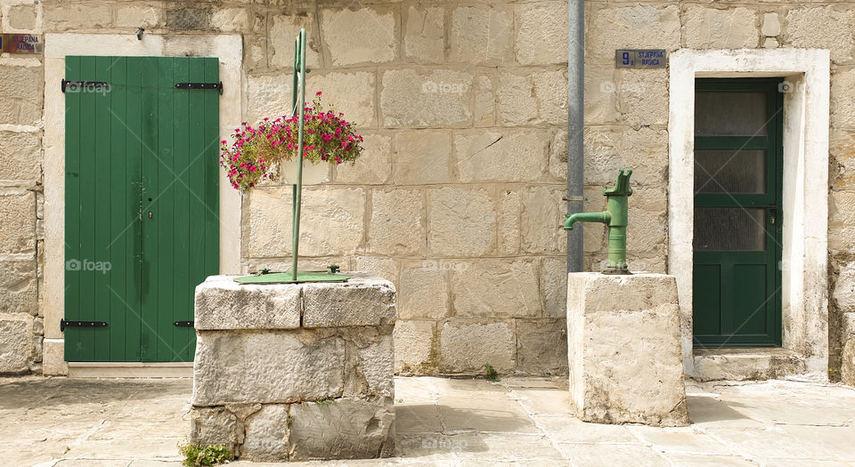 Croatia, summer landscape: a courtyard of an old stone Dalmatian bastion with a well and a water column in a Mediterranean resort town