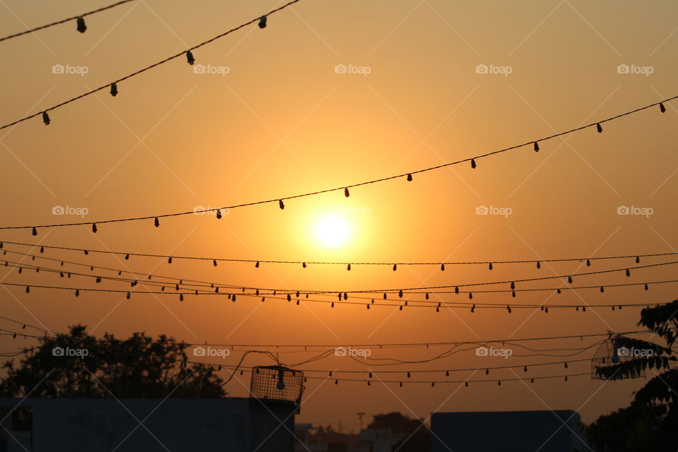 In this photo there is Artificial lighting on the roof top to decorate the roof but behind that there is a beautiful sunset which shows nature is more beautiful than manmade decoration