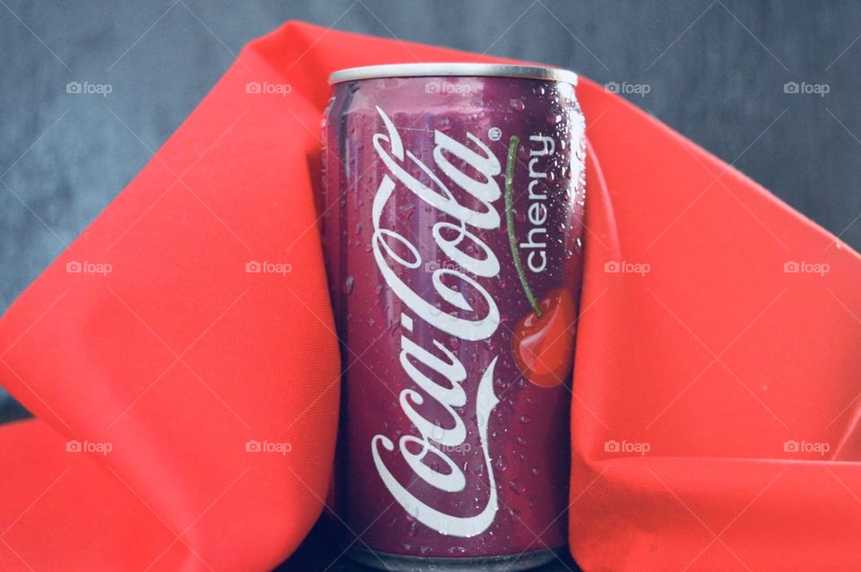 A can of cherry Coca-Cola with condensation drops on the red and with rustic background