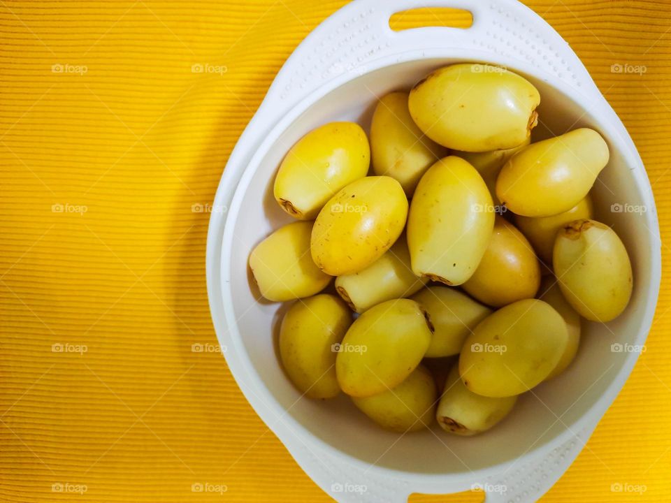 A bowl of yellow color dates in an yellow background