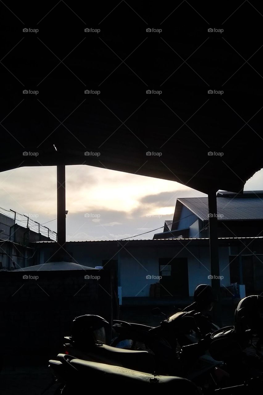 a view of the sunset or sunrise seen from under a roof, with several motorbikes parked in front of it