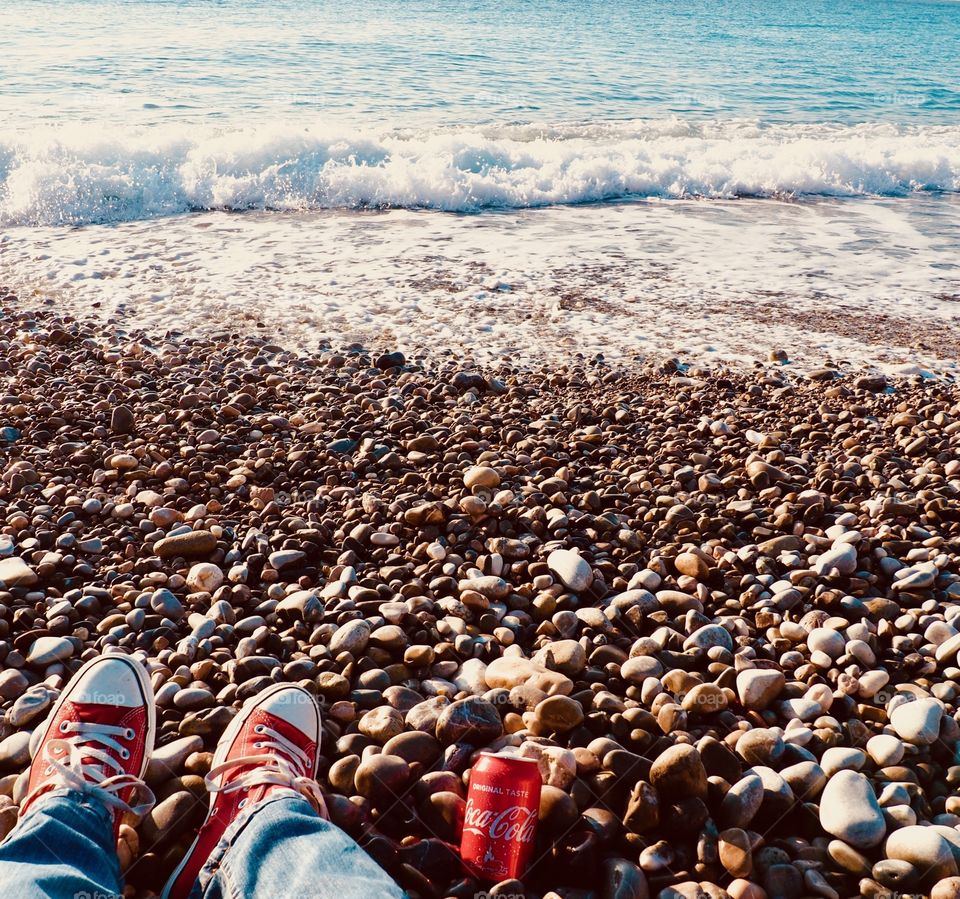 A can of Coca Cola on the beach with red sneakers.