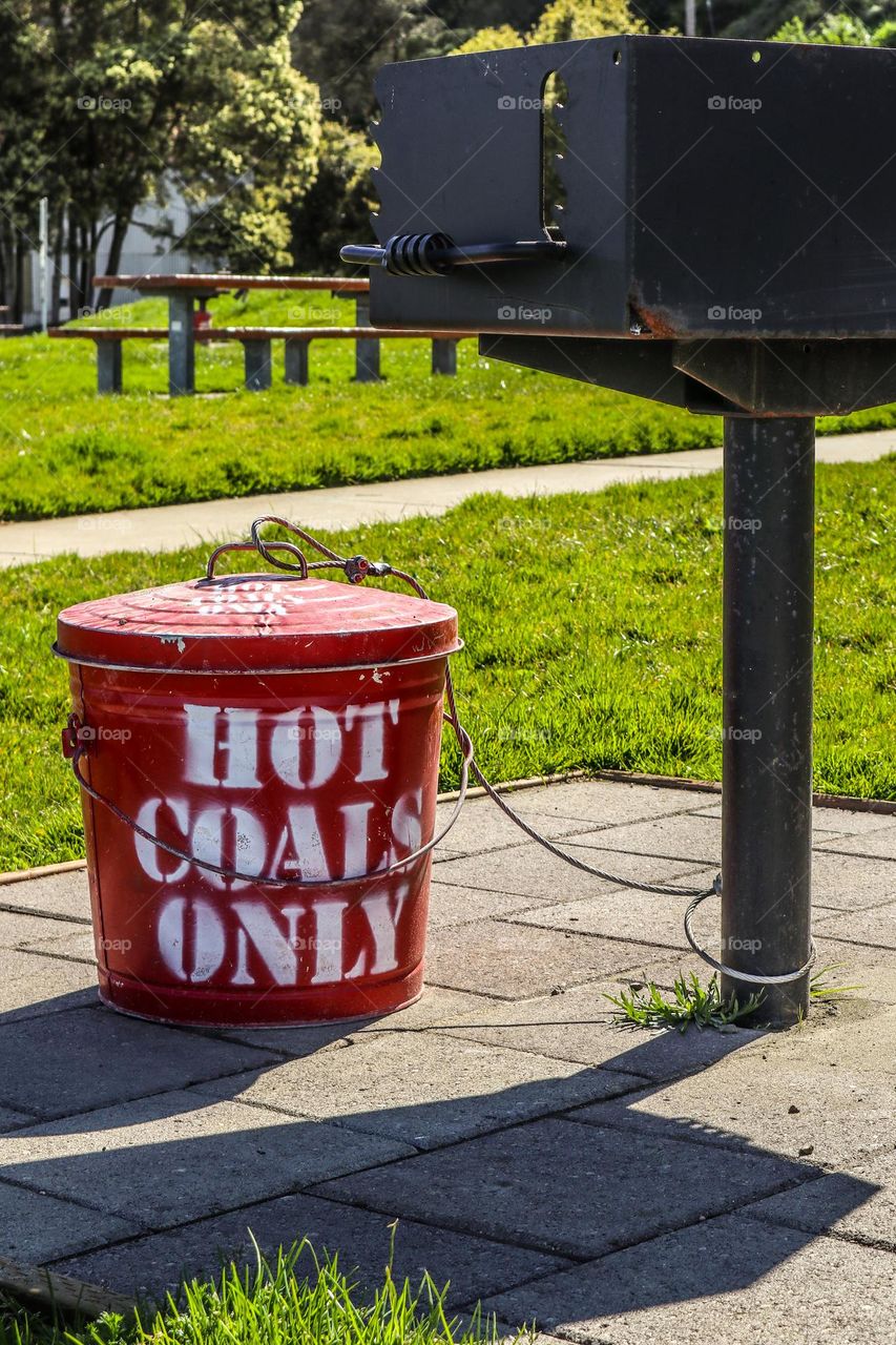 Hot coals bucket in the picnic area of Crissy Field in San Francisco California with a grill and tables and benches ready for a barbecue
