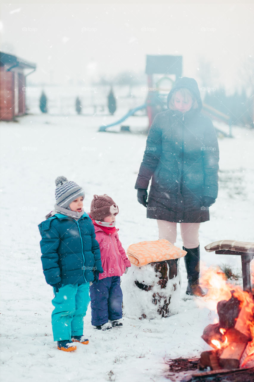 Family spending time together outdoors in the winter. Parents with children gathered around the campfire preparing marshmallows and snacks to toasting over the campfire using wooden sticks