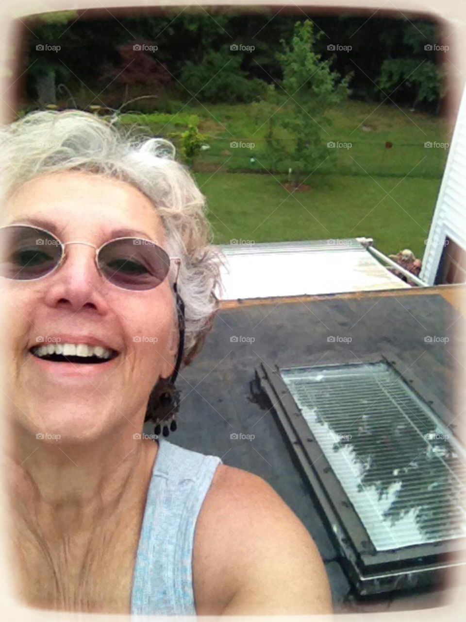 Woman on roof of house with skylight, rolled roofing part, awning over porch, backyard seen.
Hubby holding up puppy in right corner.(photobombing)