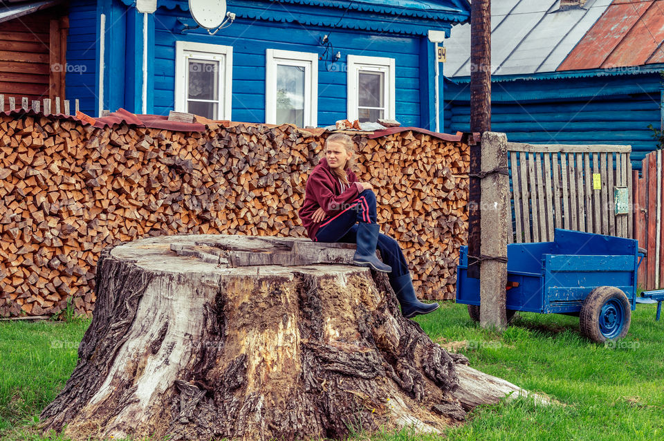 Girl is sitting on the giant stump near her rural house