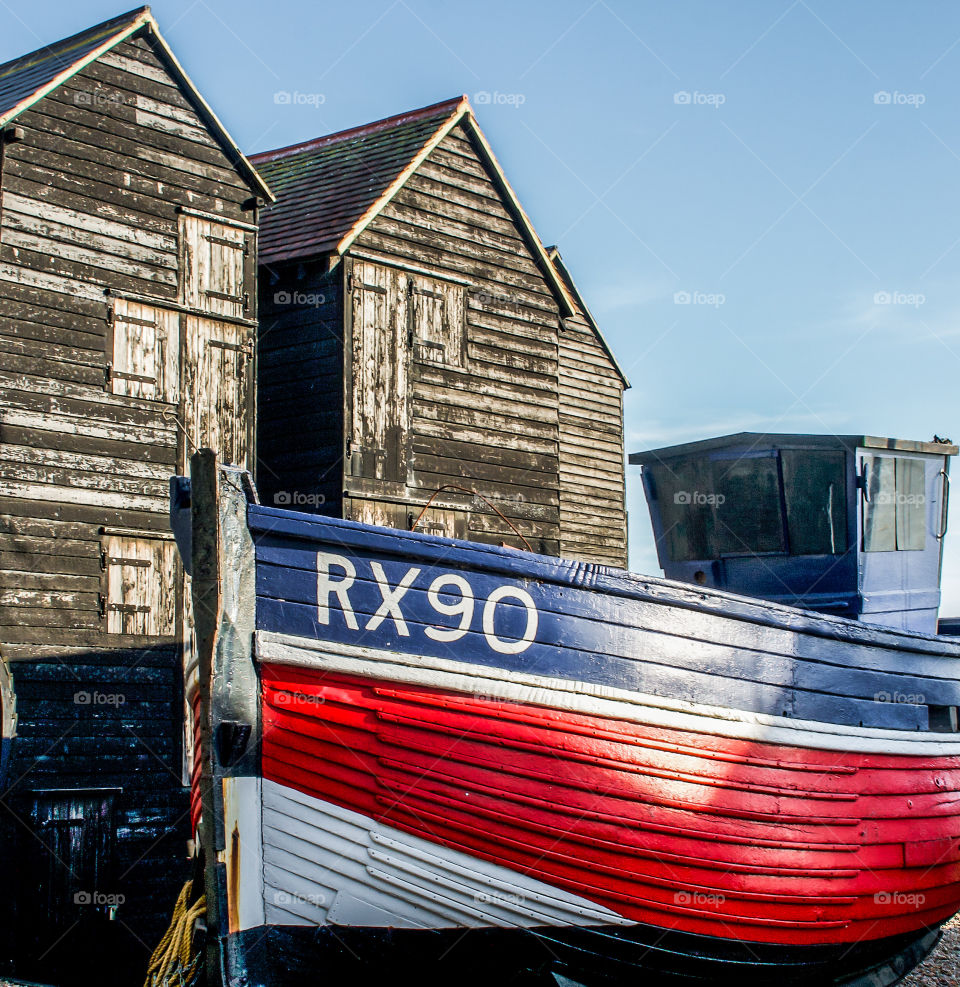 The vibrant red, painted hill of this fishing vessel, stands out against the black, wooden fishing huts that tower behind it.