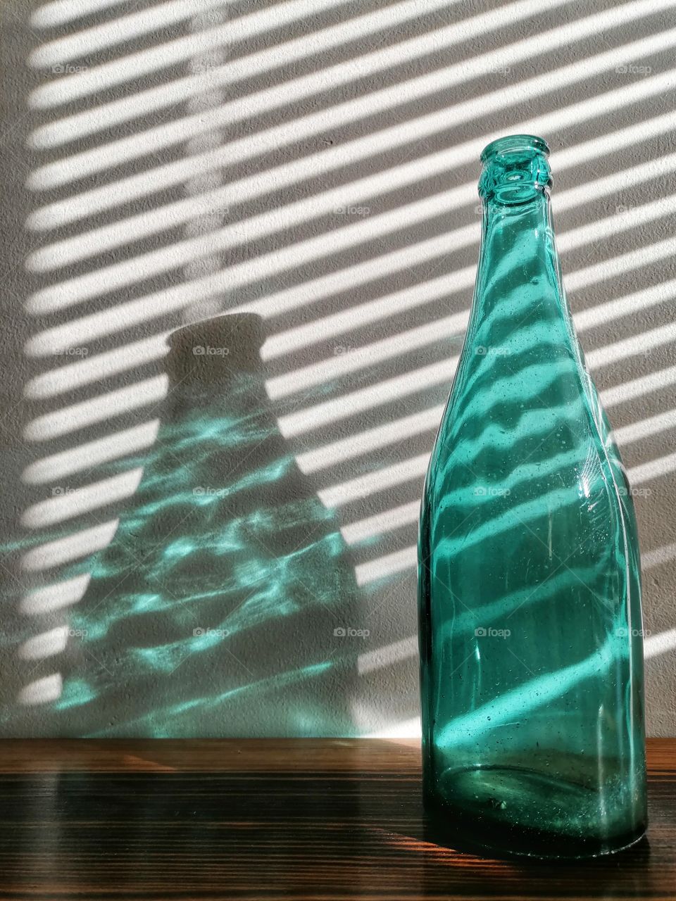 50's old blue glass bottle on a shelf. The rays of the sun between the blinds of the window bring a nice texture.