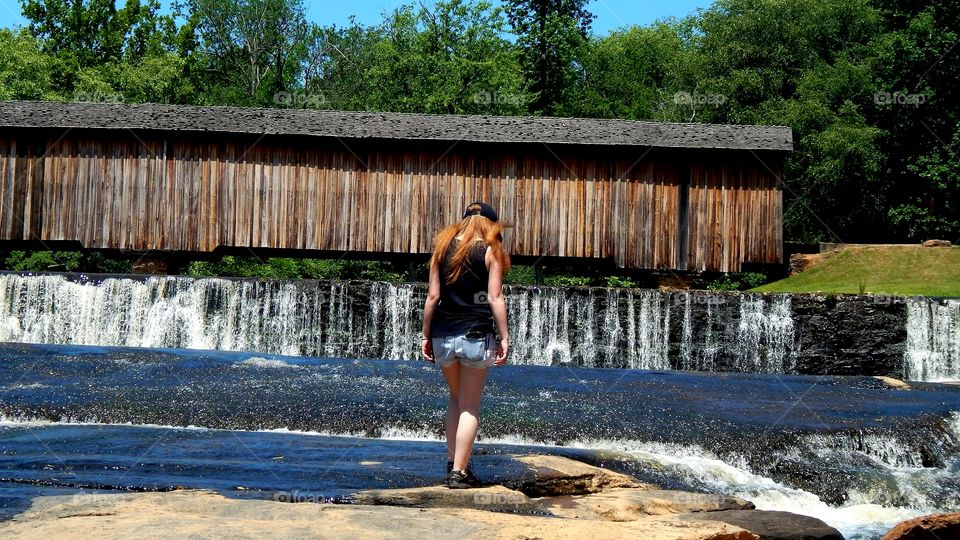 girl on rock looking at covered bridge and waterfall in Watson mill state park, Georgia