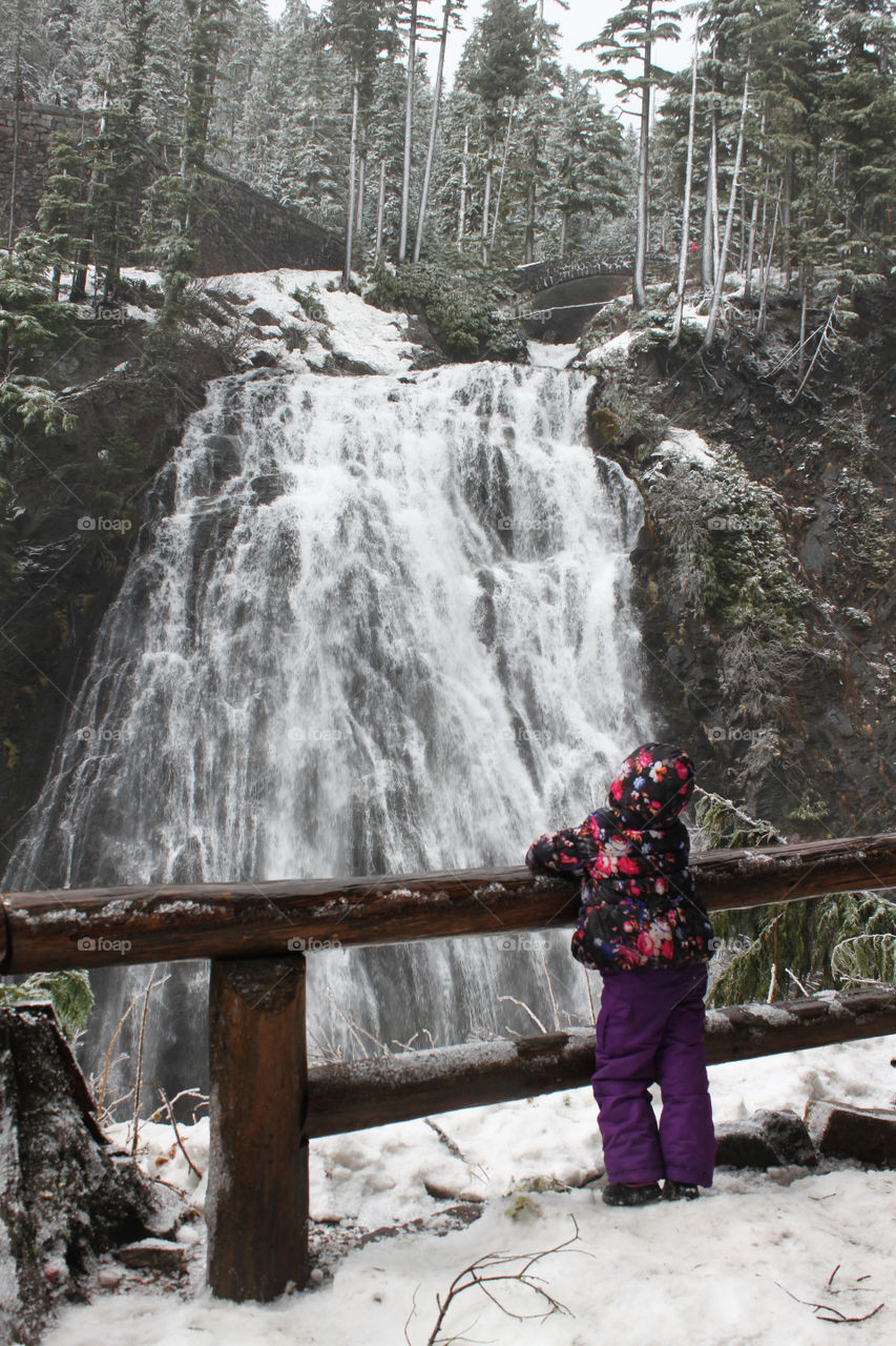 Child standing by a railing to watch a waterfall