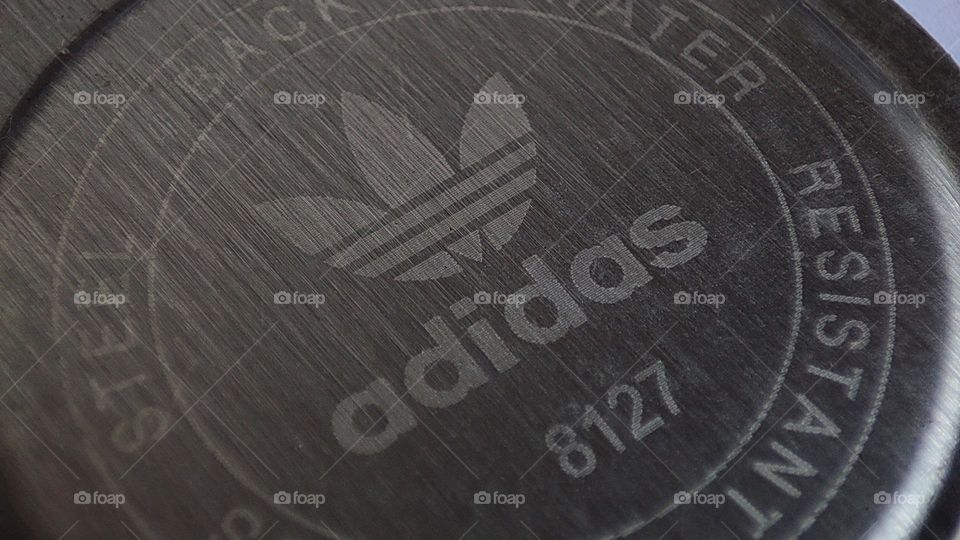 adidas logo on a metal frame, adidas logo under a watch, steal metal, stainless steel back of a watch