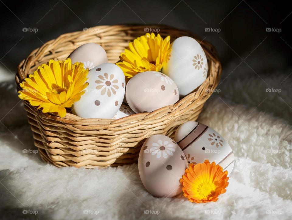 In a basket, peach & white decorated Easter eggs with yellow flowers on a soft white background 