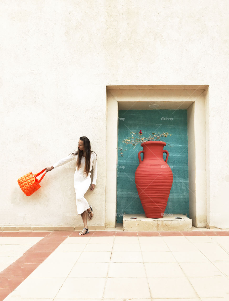 Young woman with orange purse in front of a wall with a huge orange jar