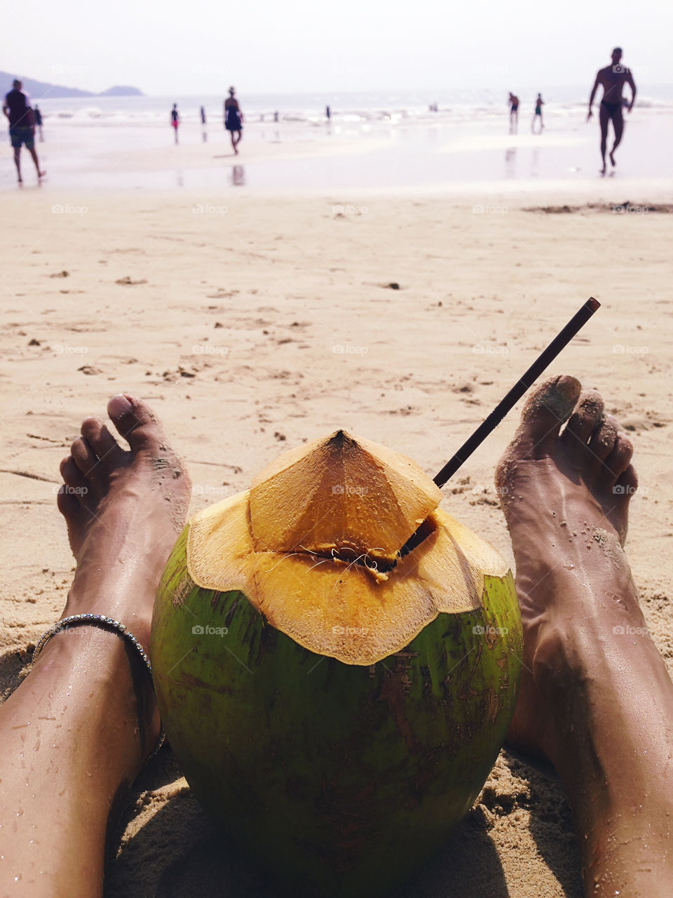 Young barefoot woman enjoying a coconut cocktail and watching reflux at the tropical sandy beach 