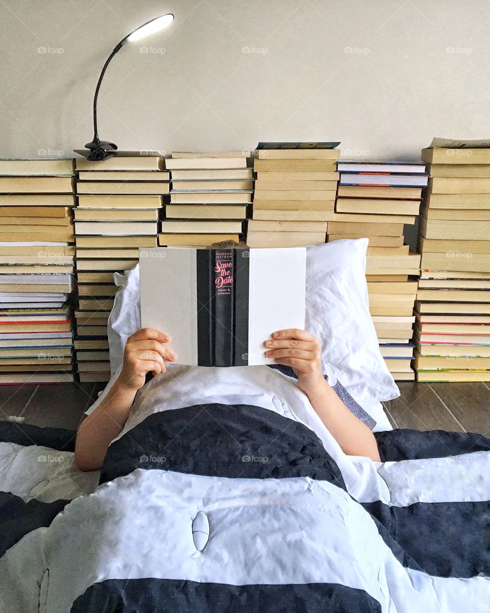 Person reading in a bed created from books. 