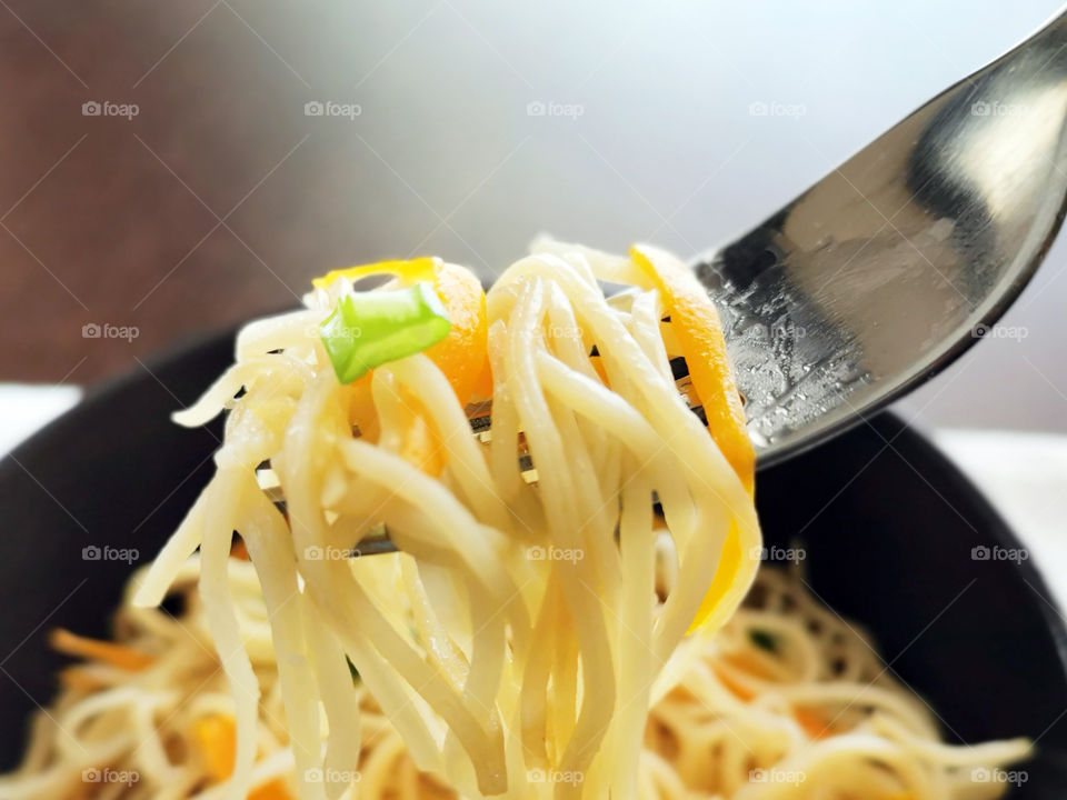Chow mein with vegetables on a fork. Selective focus at the noodles on the fork after the spring onion.