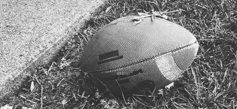 black and white close-up view of an American Football lying upside down in the grass