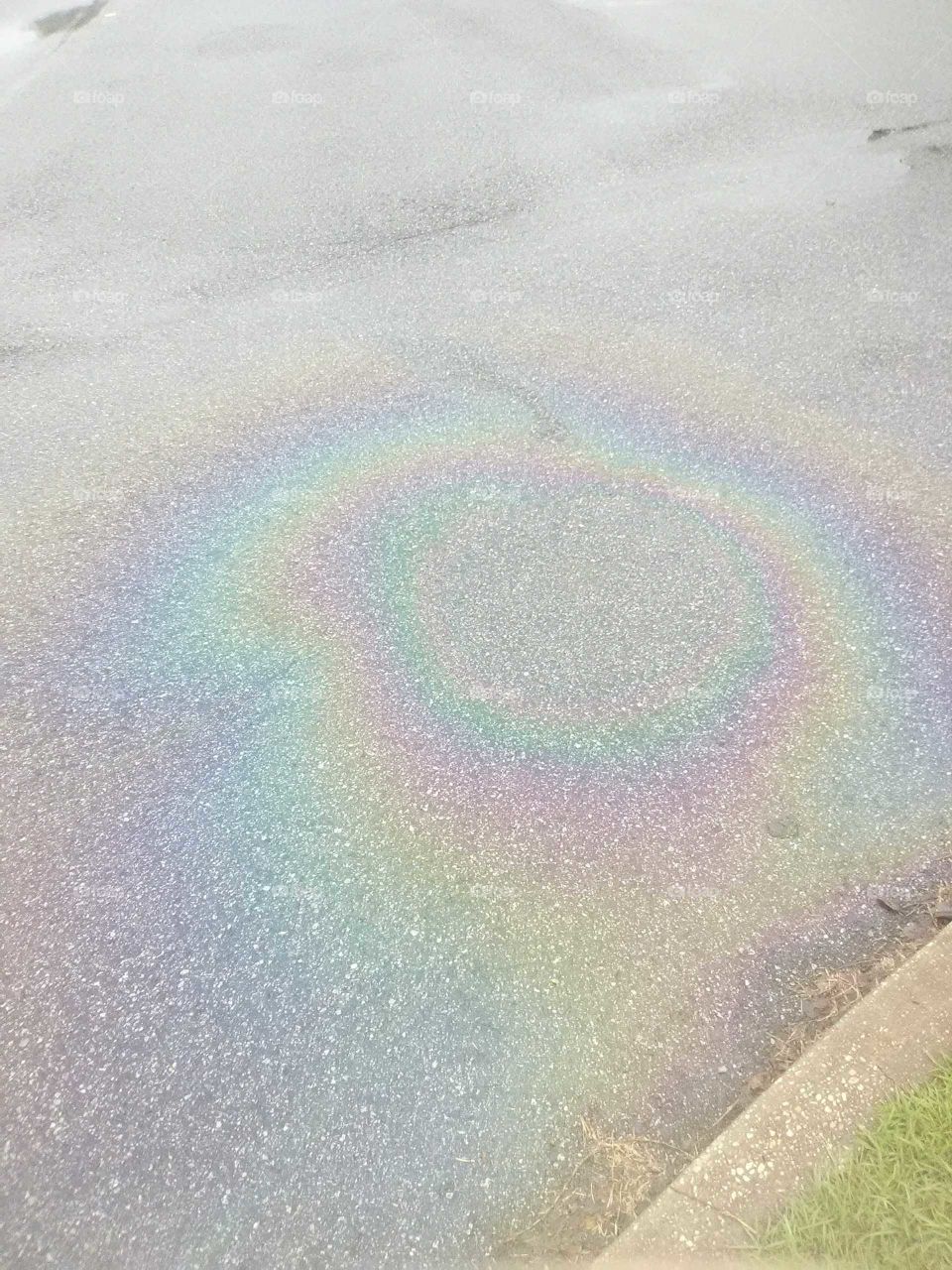 rainbow oil cirlce on asphalt with sidewalk in the background.