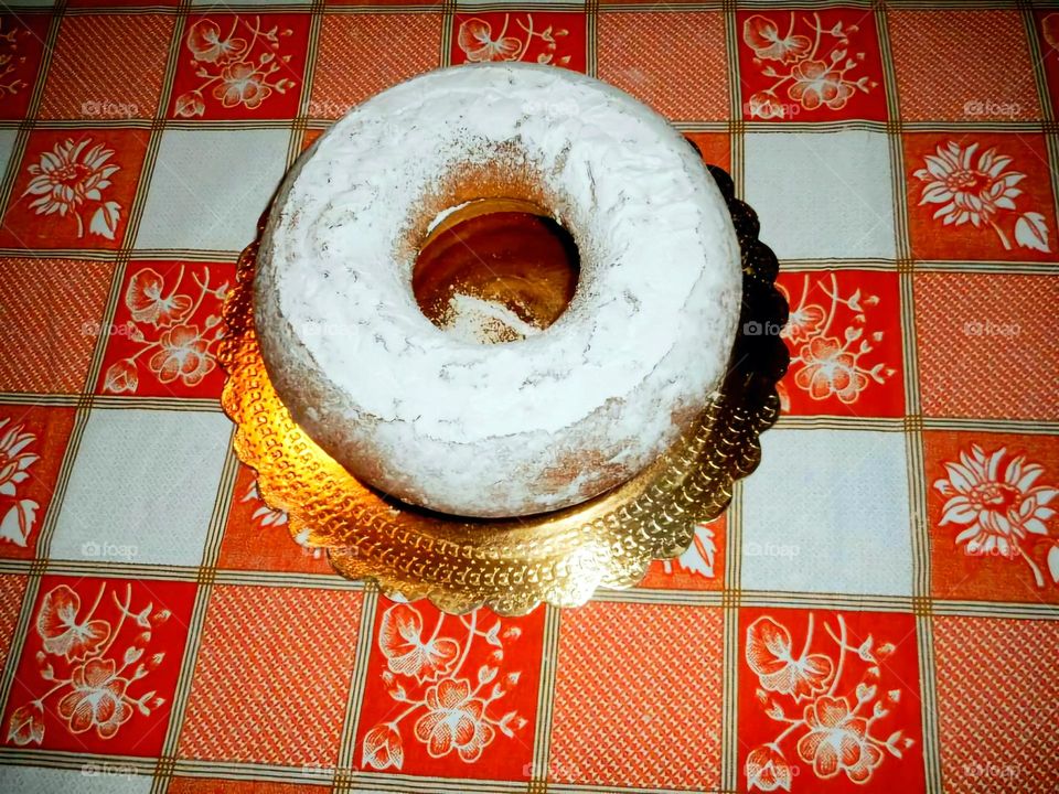 Homemade bundt cake with a sprinkle of powdedered sugar on a  checkered tablecloth