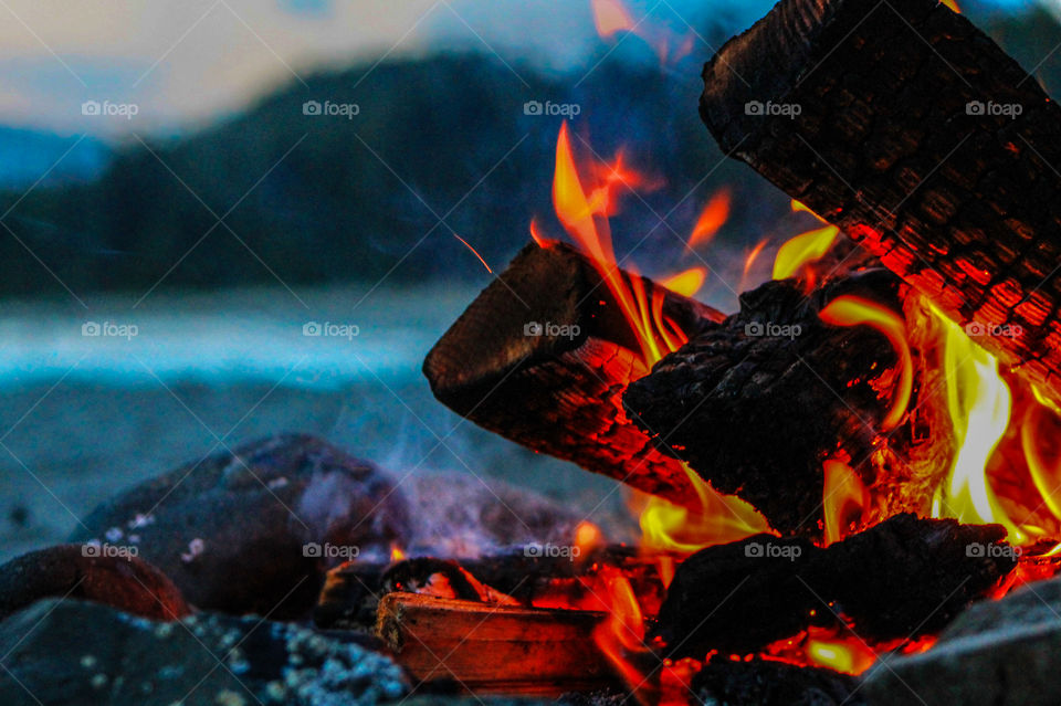 The beautiful natural light of a beach fire against a  darkening sky. The world transformed as the sun set behind the mountains & the flames & smoke from the fire danced in the air creating a myriad of colours. 