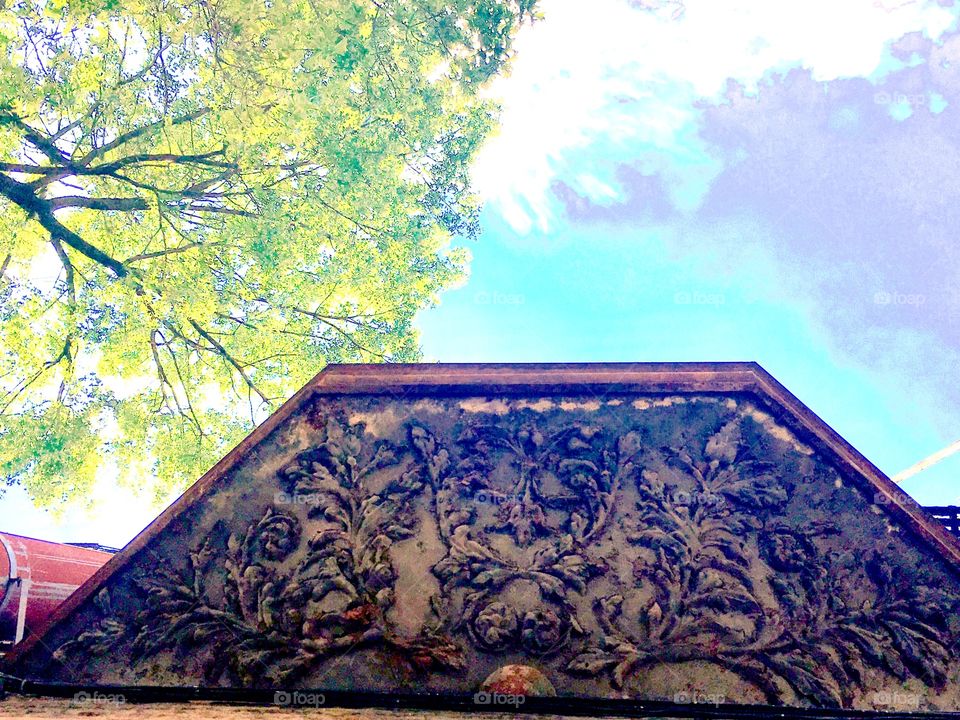 The underside of an antique wooden awning with interesting ornamentation to a first floor window of an abandoned building on Waverly Street just off Fulton Street in Brooklyn, New York. Photographed looking up into the sky in the summer of 2019.
