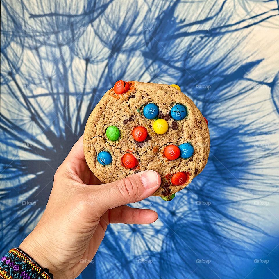 Woman’s hand holding M&M cookie, eating desserts on vacation, M&M cookie sandwich with icing 