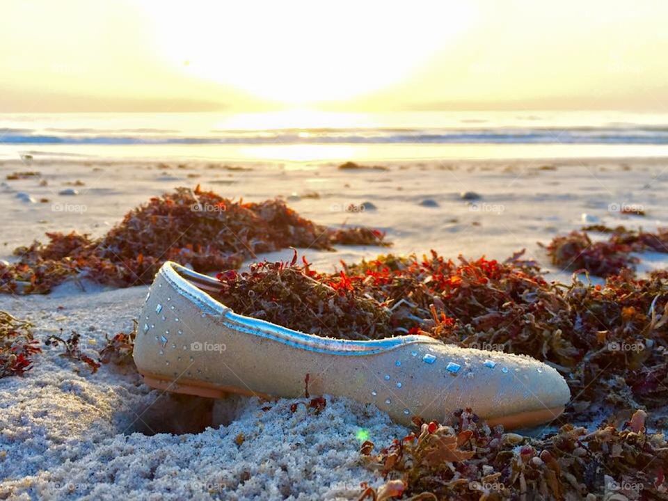 Cinderella goes to the beach.  Satin shoe. Fancy slipper. Beachwear. All that glitters. Sunshine. Seashore. Sparkles. 