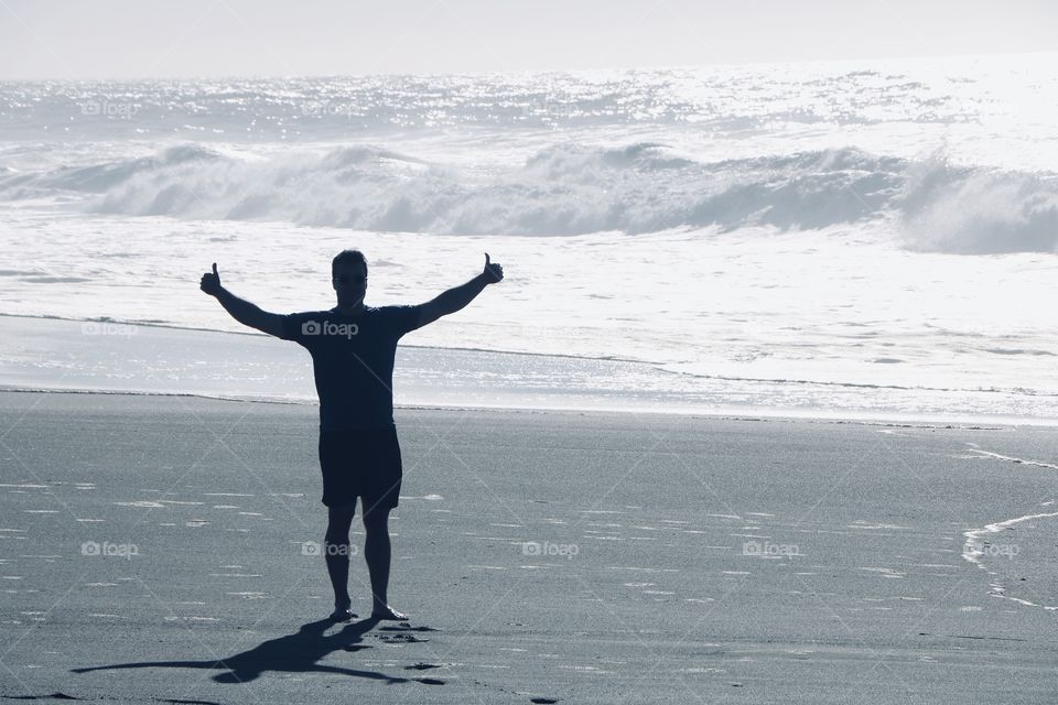 Happy man by the stormy ocean , it’s shadow casting in the sand 