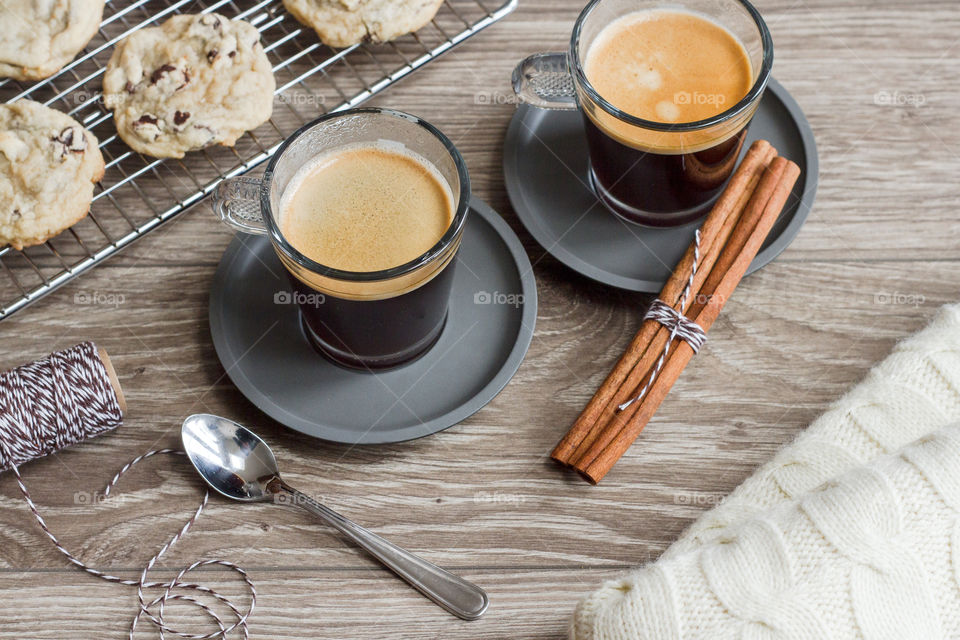 Two warm cups of espresso coffee styled with freshly baked goods and a warm blanket