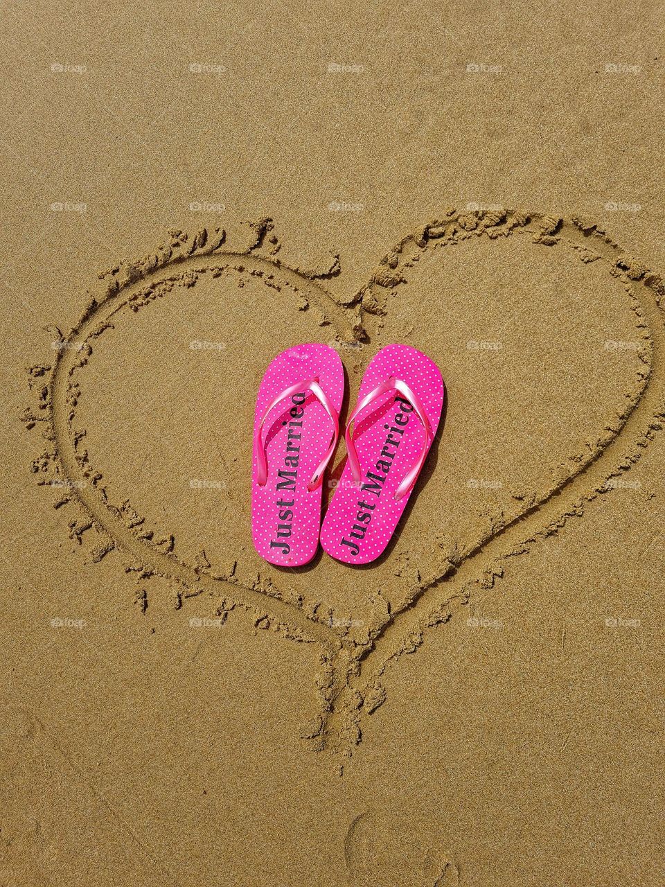 bright pink slip slips with the word "just married" on them, on the beach sand with a heart drawn around it