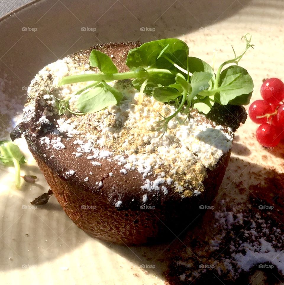 Chocolate fondant covered with golden dust and powdered sugar with red currants served in Riga, Latvia