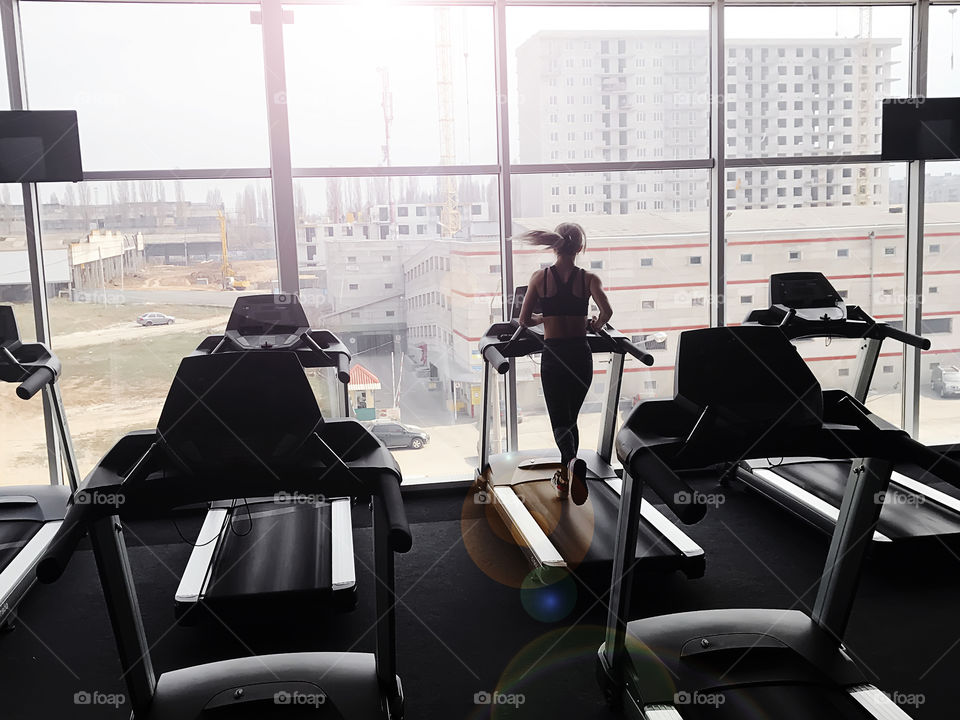 Silhouette of a young woman running at the gym with a city view 