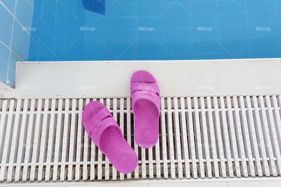 Pink slippers for swimming stand near the pool with blue water.