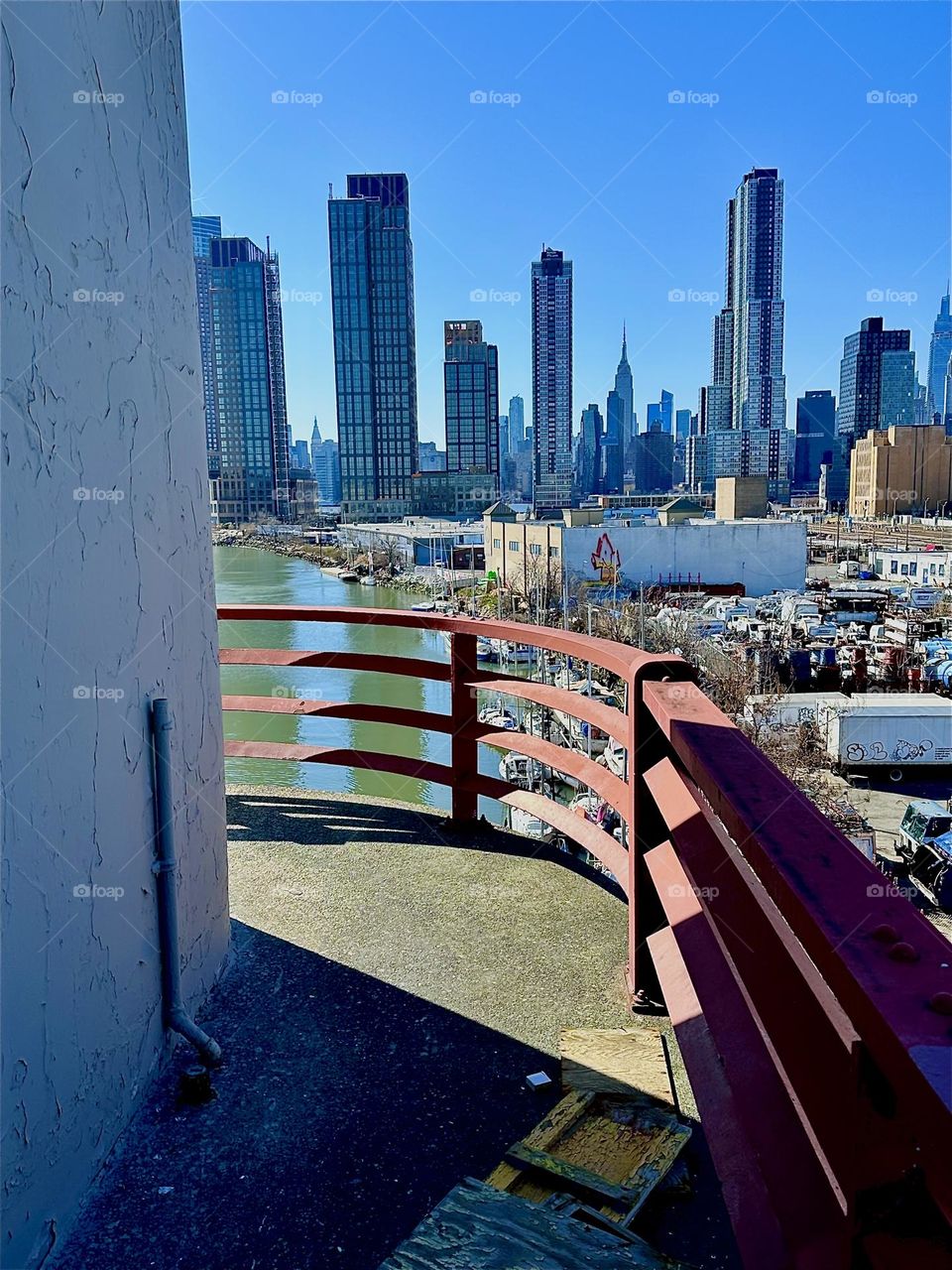 This is the central outpost of the „Pulaski Bridge“ that connects LIC to „Greenpoint“, Bklyn overlooking „Newtown Creek“, ocean inlet of the „E River“. In the distance we see „Manhattan“ including the „Empire State Bldg“. 2024. Hypnotic Productions