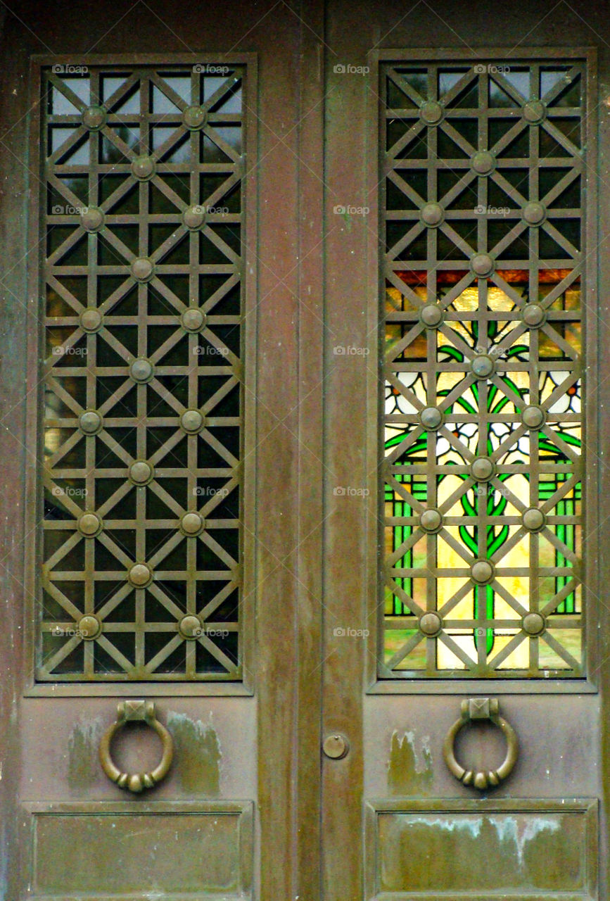A beautiful stained glass window can be seen through the doors of a mausoleum.