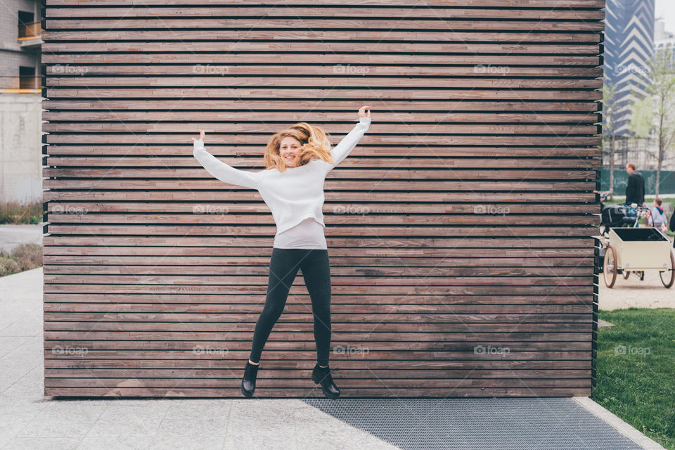 Happy young blonde woman with white shirt jumping in the street - happiness, freedom